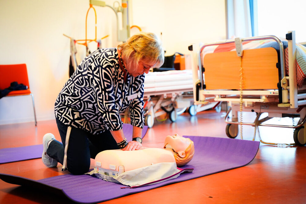 Eine Ausbilderin kniet über einer Puppe im Skills Lab und reanimiert diese